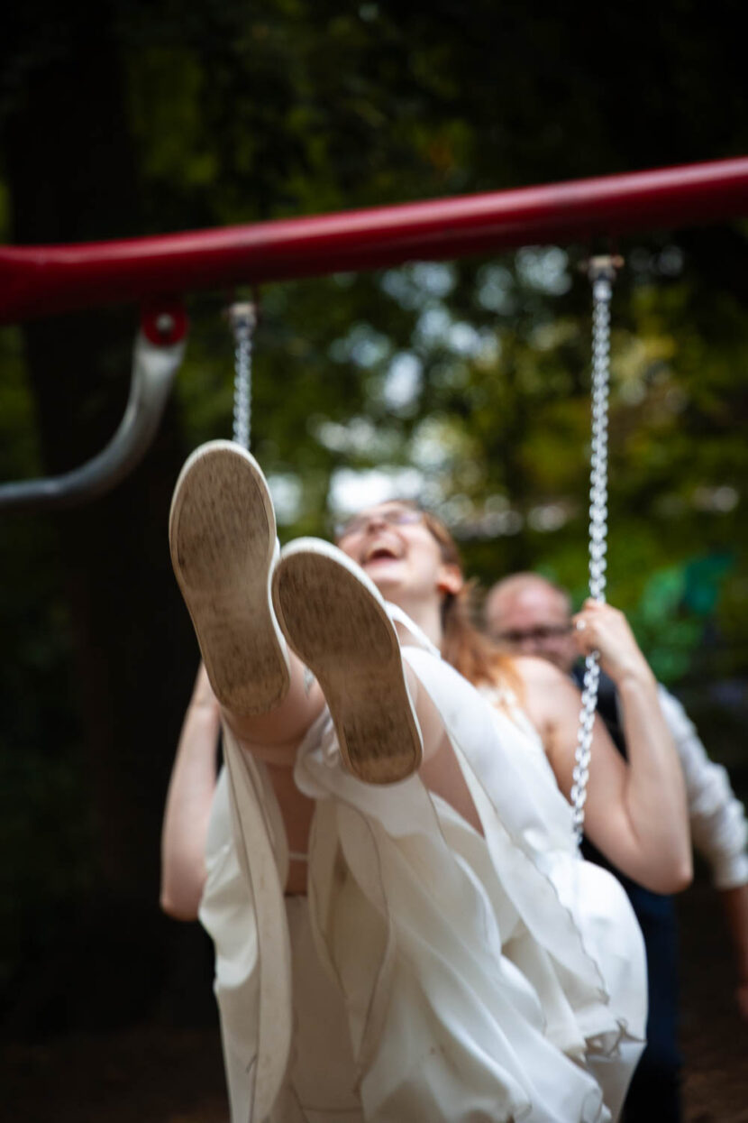 Braut schwingt auf der Schaukel im Flößerpark in Richtung Kamera.